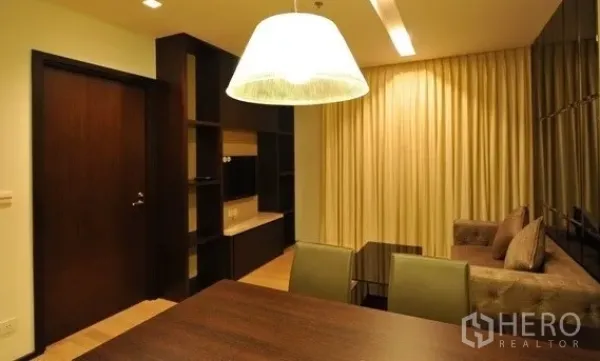 公寓 出租在Khlong Toei, Bangkok - 从餐区望向客厅的视角，带内置书架、大型吊灯与窗帘