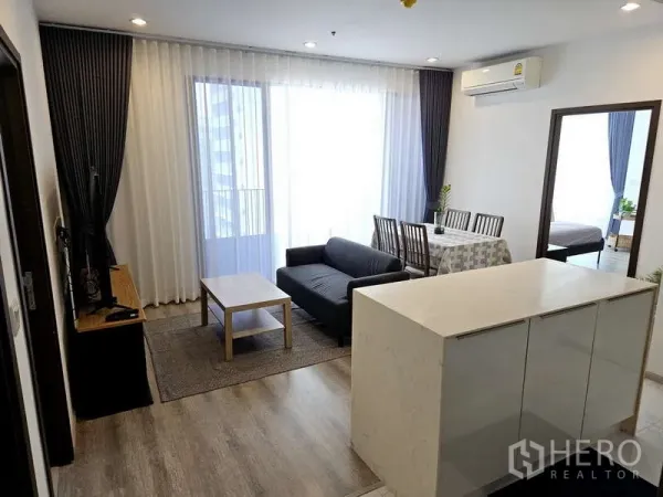 公寓 出租在Bang Na, Bangkok - 采光充足的起居区，落地窗与阳台，配餐桌与空调，邦纳现代公寓。