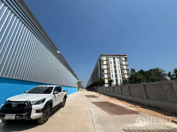 Warehouse for rent in Lat Krabang, Bangkok - Access road with on-site parking beside a metal-clad warehouse and nearby low-rise residential building.