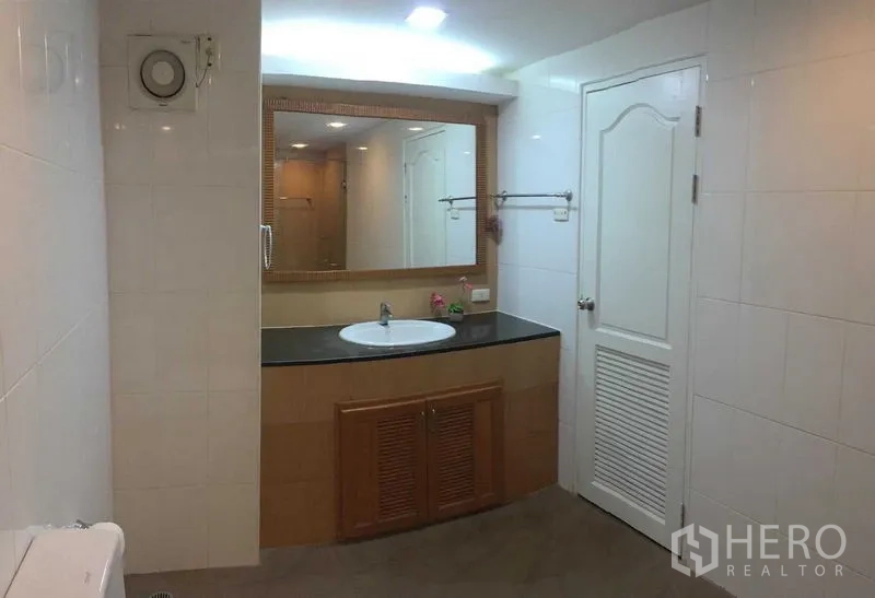 Condominium for rent or sale in Din Daeng, Bangkok - Spacious bathroom featuring a large mirror, single-sink vanity with black countertop and tiled walls.