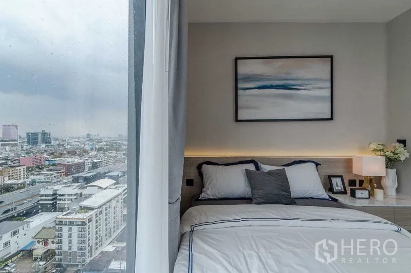 Condominium for rent in Pathum Wan, Bangkok - Cozy bedroom with wide window, nightstand lighting and sweeping Bangkok city view.