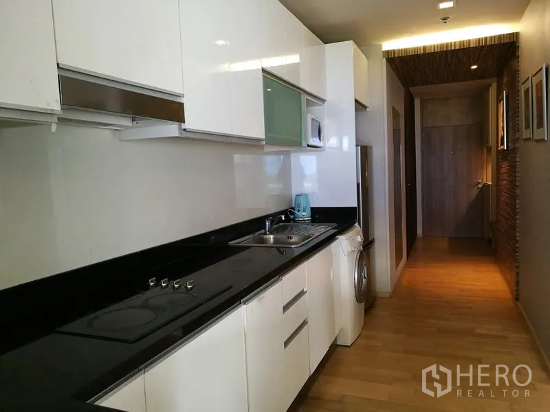 คอนโด ให้เช่าในWatthana, Bangkok - ครัวแบบแกลลีย์ ตู้สีขาวเงา ท็อปหินสีดำ เตาไฟฟ้า อ่างล้างจาน และเครื่องซักผ้าในตัว
