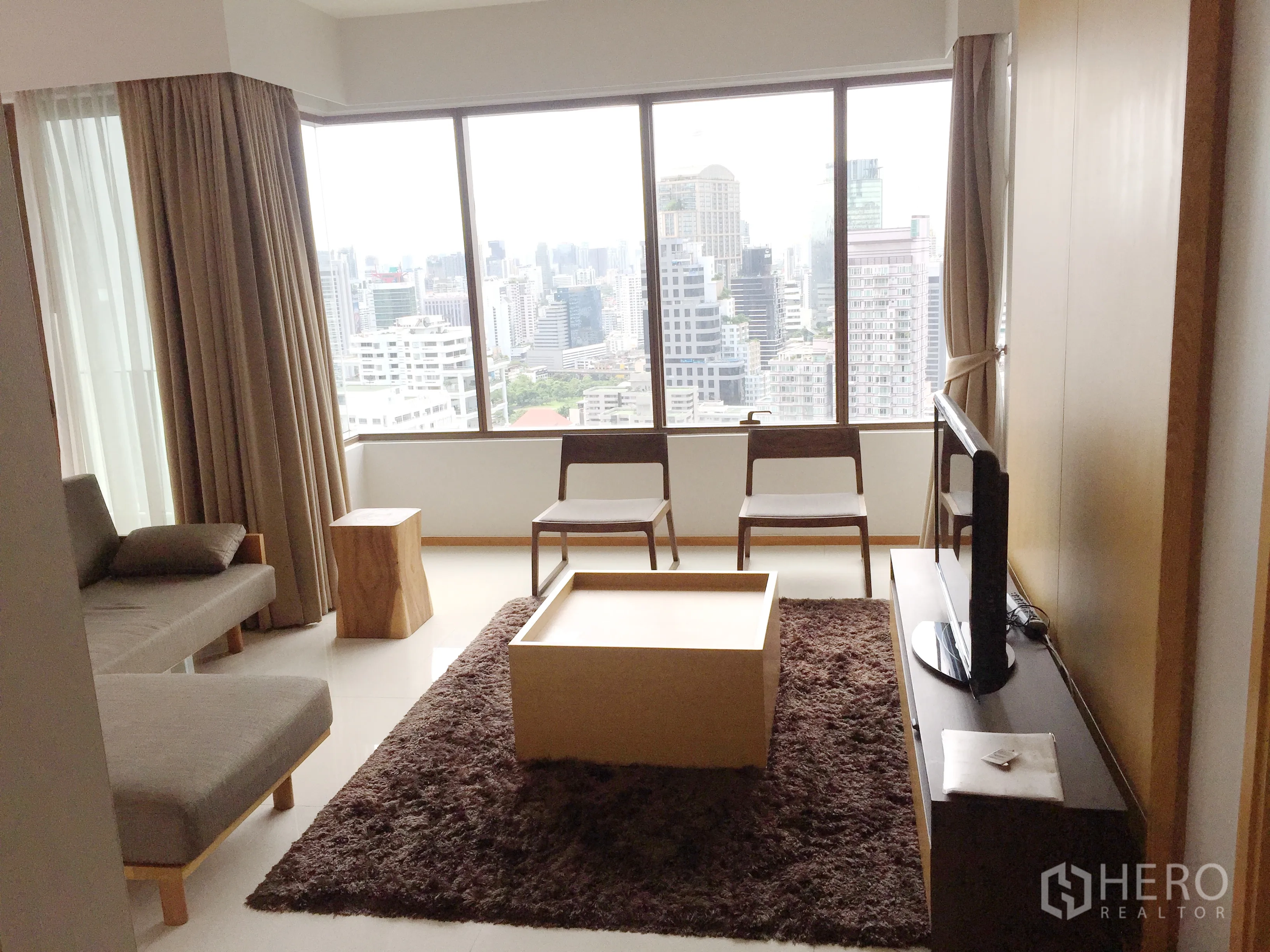 Condominium for rent in Khlong Toei, Bangkok - Cozy living room with sofa, TV unit, and large windows offering natural light and city views.