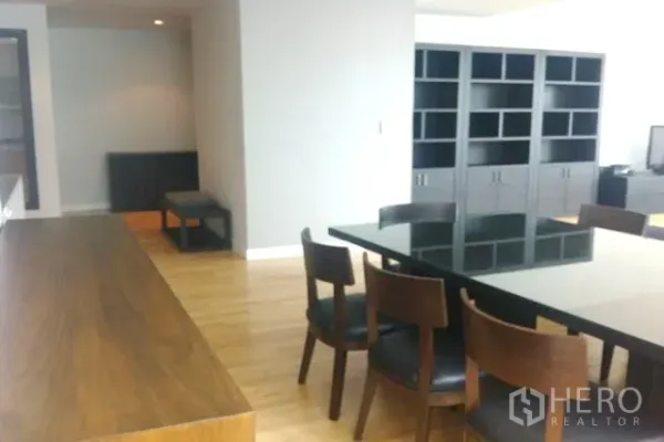 Condominium for sale in Khlong Toei, Bangkok - Open-plan dining area with black glass-top table and wooden chairs beside a long breakfast bar and built-in shelves.