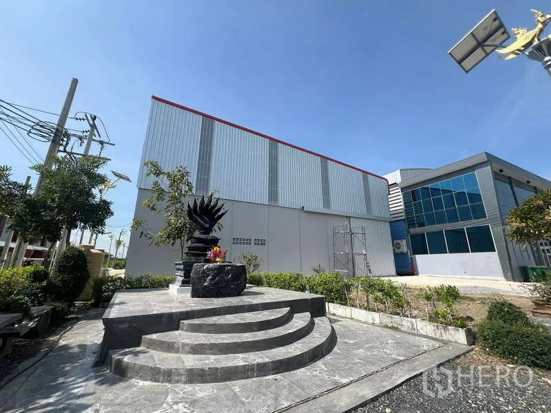 货栈 出租在Prawet, Bangkok - 金属板外墙的仓库外观，旁有景观花园与石质平台。