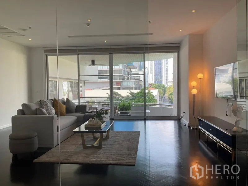 Apartment for rent in Sathon, Bangkok - Sitting room behind a glass wall opening to a wide terrace with greenery.