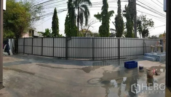 คลังสินค้า ให้เช่าในSai Mai, Bangkok - รั้วรอบที่ดินแบบแผ่นเมทัลชีท ด้านนอกมีต้นปาล์มและทางเทคอนกรีต.