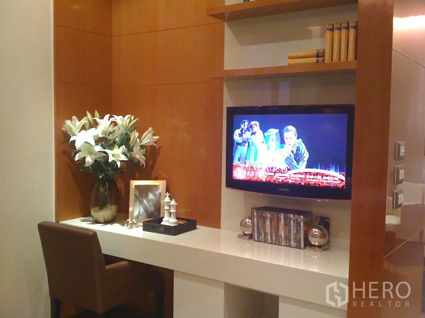 Condominium for rent or sale in Khlong Toei, Bangkok - Built-in study nook with desk, shelving, flat-screen TV, and vase of lilies in a contemporary condo.