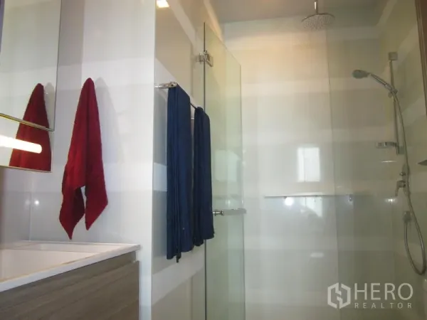 Condominium for rent in Khlong Toei, Bangkok - Contemporary bathroom with glass shower enclosure, rainfall showerhead, handheld sprayer and striped wall tiles.