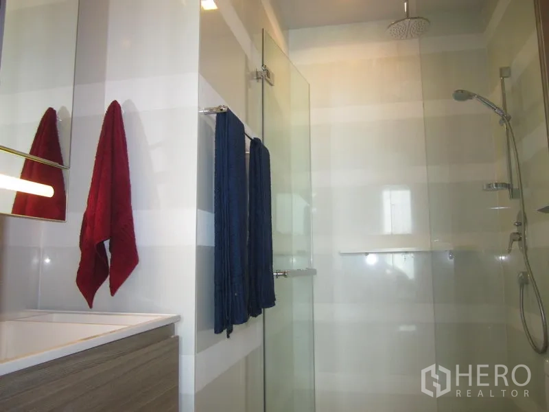 Condominium for rent in Khlong Toei, Bangkok - Contemporary bathroom with glass shower enclosure, rainfall showerhead, handheld sprayer and striped wall tiles.