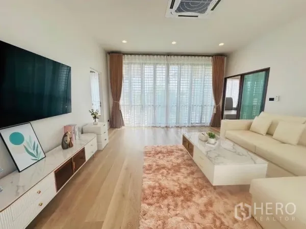 Detached House for rent or sale in Bang Kapi, Bangkok - Spacious living area with L‑shaped sofa, marble coffee table, recessed lights and large window wall with sheer curtains.