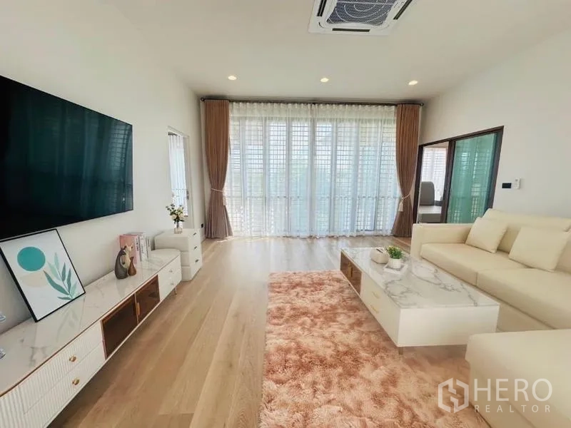 Detached House for rent or sale in Bang Kapi, Bangkok - Spacious living area with L‑shaped sofa, marble coffee table, recessed lights and large window wall with sheer curtains.
