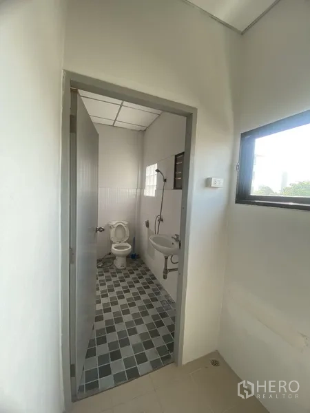 Townhouse for rent in Suan Luang, Bangkok - Compact bathroom with shower, toilet and sink, featuring checkered floor tiles and window.