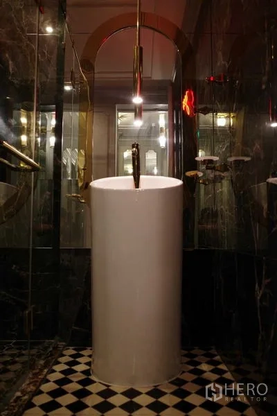 Condominium for sale - Luxurious bathroom with pedestal sink, glass shower and dark marble walls.
