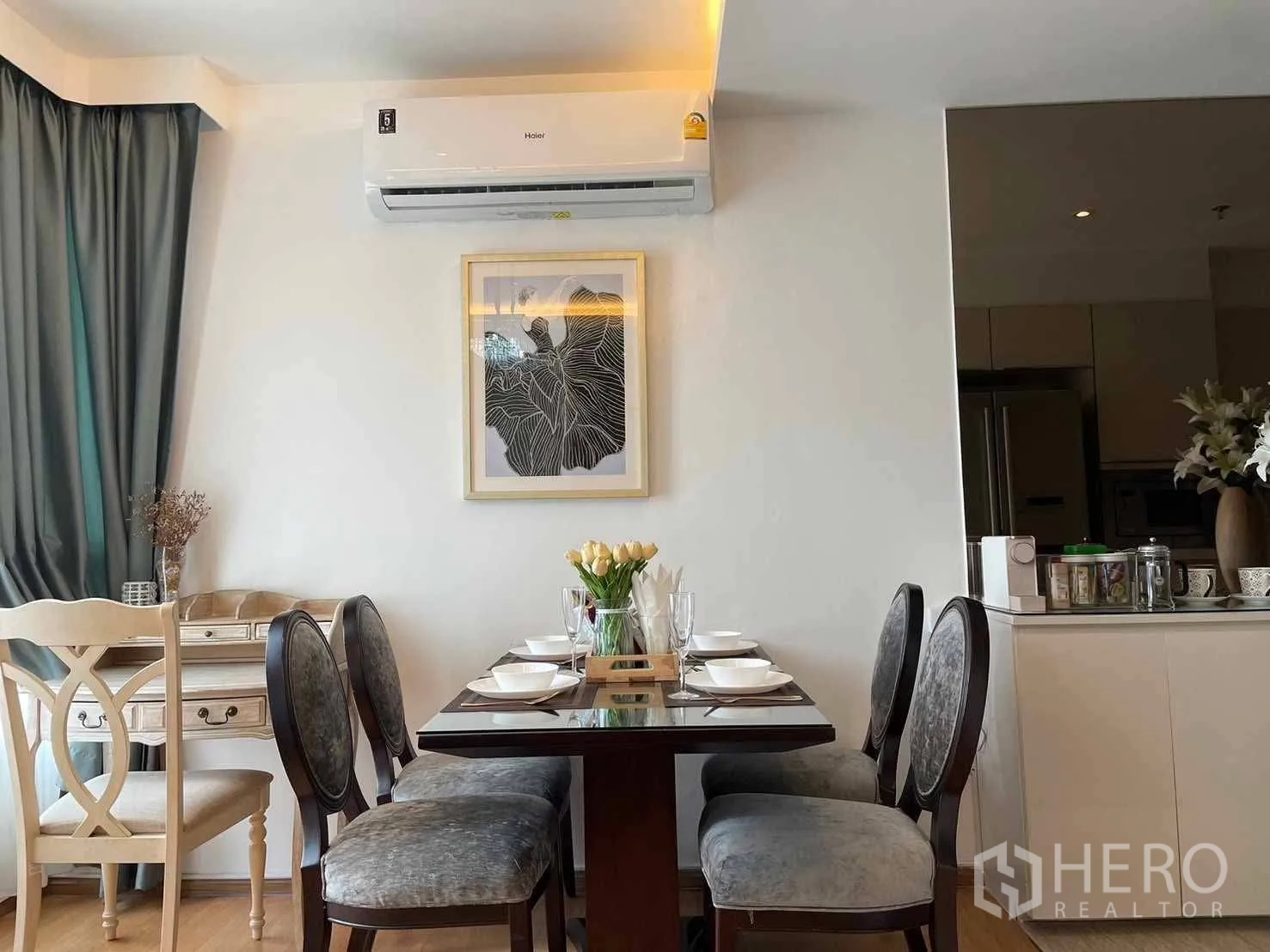 Condominium for rent in Watthana, Bangkok - Dining area with four-seat table, wall air-conditioner, and draped windows next to the kitchen.