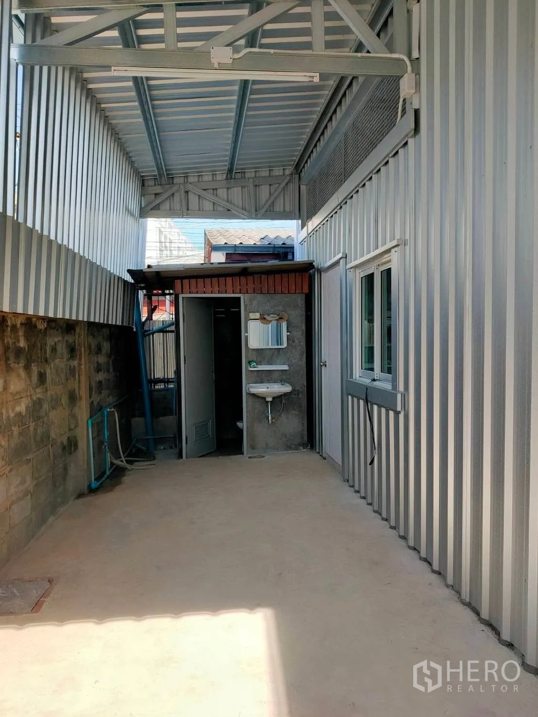 Warehouse for rent in Lat Phrao, Bangkok - Covered side passage showing restroom doors, a wall-mounted sink, and metal cladding.