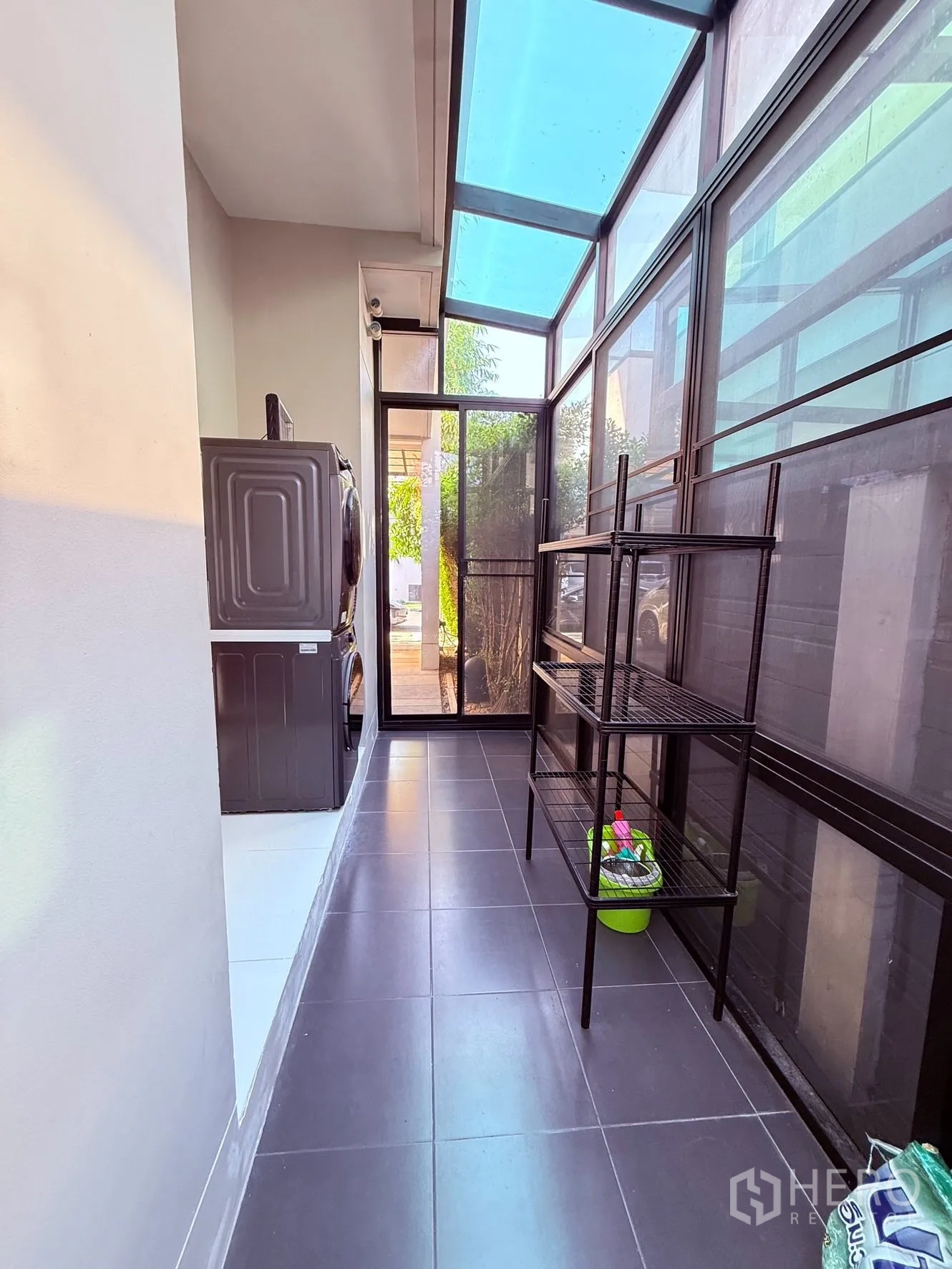 Detached House for rent or sale in Prawet, Bangkok - Enclosed laundry area with glass roof, washer and dryer, and metal storage shelves.