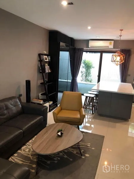 Townhouse for rent in Lat Phrao, Bangkok - Open-plan lounge leading to a patio via sliding glass doors, with air-con and dining island.