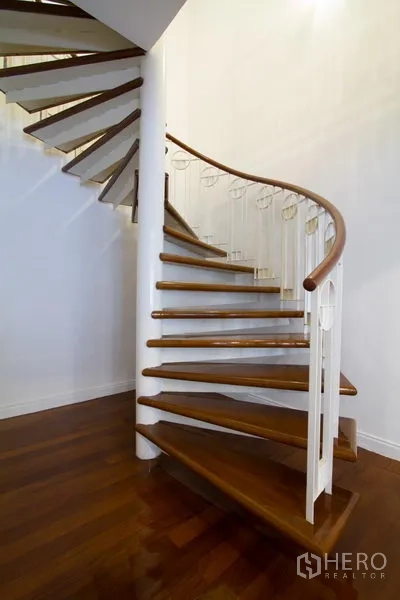 Apartment for rent in Watthana, Bangkok - Close-up of a wooden spiral staircase with white balustrade and dark wood treads.