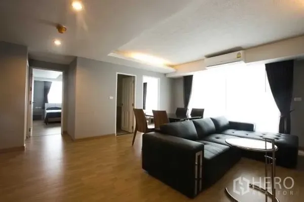 Condominium for rent in Khlong Toei, Bangkok - Open-plan lounge with sectional sofa, round side table and dining set by a large window.