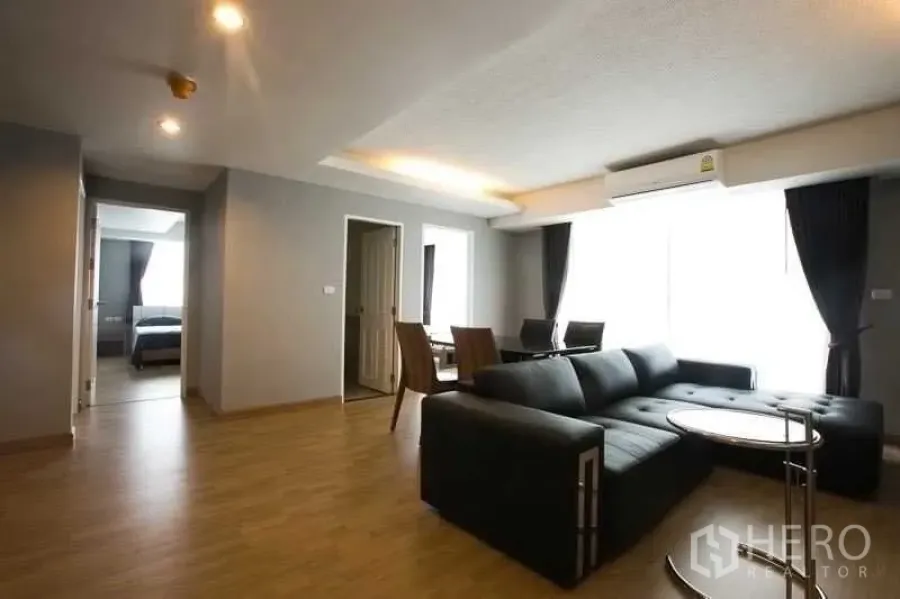 Condominium for rent in Khlong Toei, Bangkok - Open-plan lounge with sectional sofa, round side table and dining set by a large window.