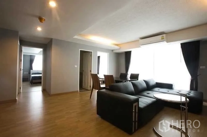 Condominium for rent in Khlong Toei, Bangkok - Open-plan lounge with sectional sofa, round side table and dining set by a large window.