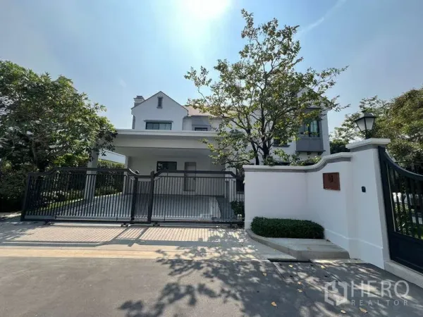 บ้าน ให้เช่าในSaphan Sung, Bangkok - มุมหน้าบ้านสองชั้นสีขาวสไตล์โมเดิร์น พร้อมประตูรั้วและทางรถยนต์มีต้นไม้ร่มรื่น