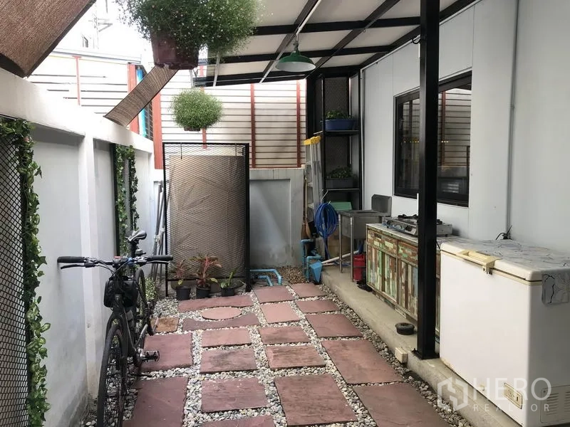 Townhouse for rent in Saphan Sung, Bangkok - Covered utility patio with stepping stones, hanging plants, storage shelves and a bicycle