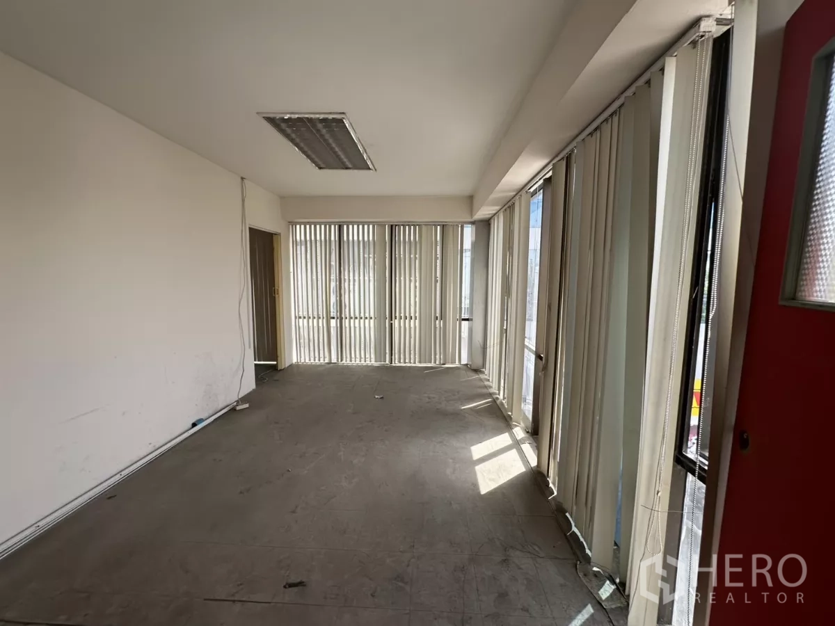 Warehouse for rent in Suan Luang, Bangkok - Narrow office room with vertical blinds letting in natural light beside a red door.