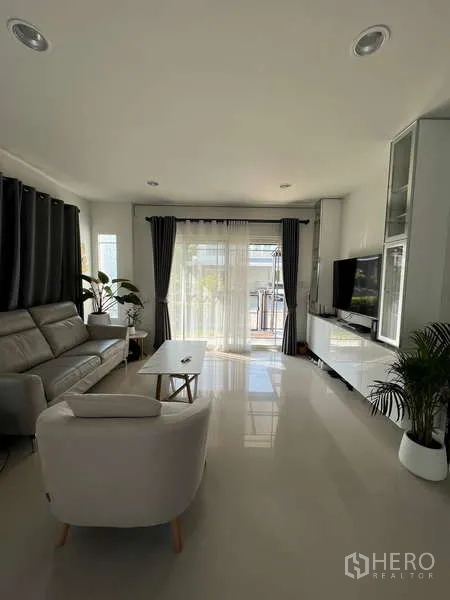 Detached House for rent in Bang Kapi, Bangkok - Sunlit living room with sofa set, TV wall and sliding glass doors.