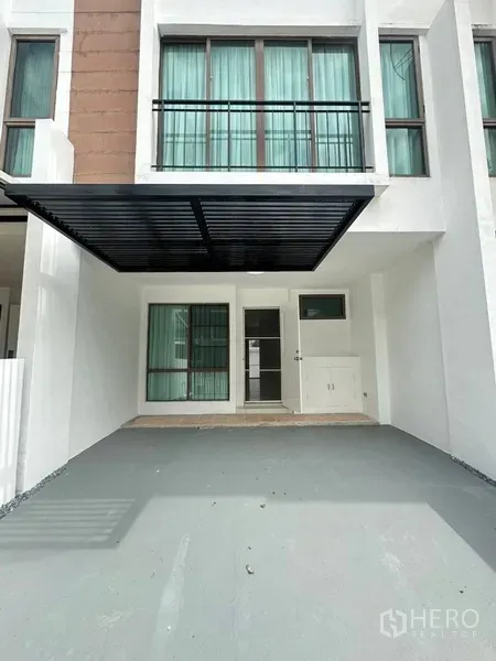 Townhouse for rent or sale in Phra Khanong, Bangkok - Covered carport and entrance with large windows and green curtains.