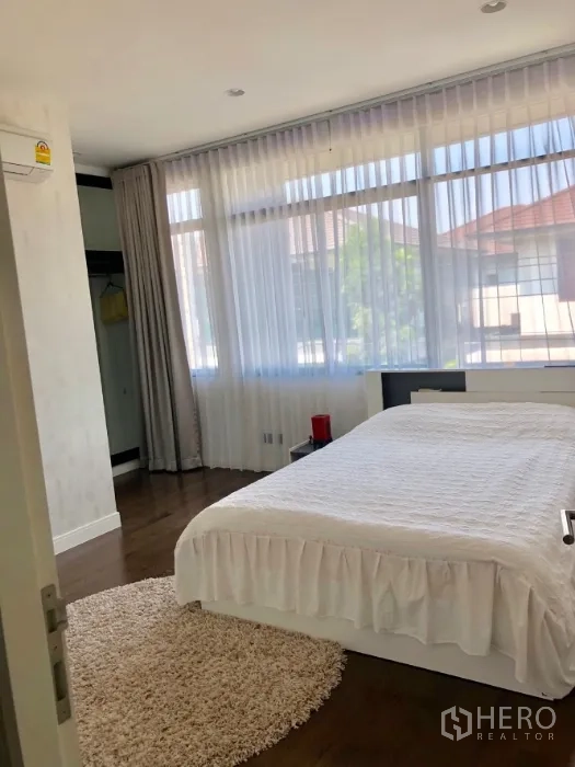 Detached House for rent in Bang Kapi, Bangkok - Bright secondary bedroom with large windows, sheer curtains and white bedding on wood floors.