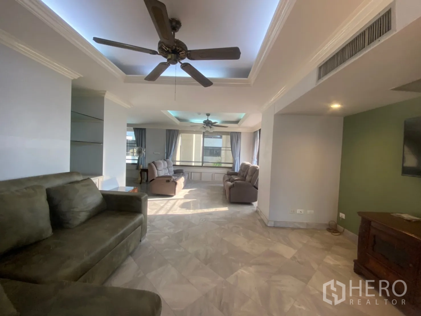 Condominium for rent or sale in Watthana, Bangkok - Open living area with cove lighting, ceiling fan and windows facing the skyline.