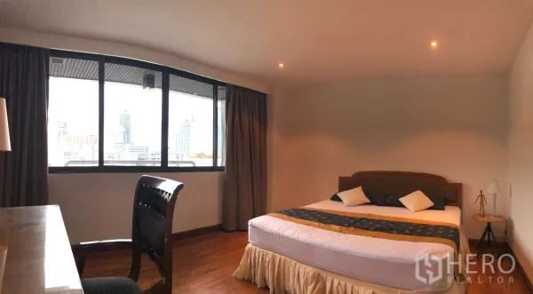 Condominium for rent in Khlong Toei, Bangkok - Master bedroom with king bed, desk and large window overlooking the Bangkok skyline.
