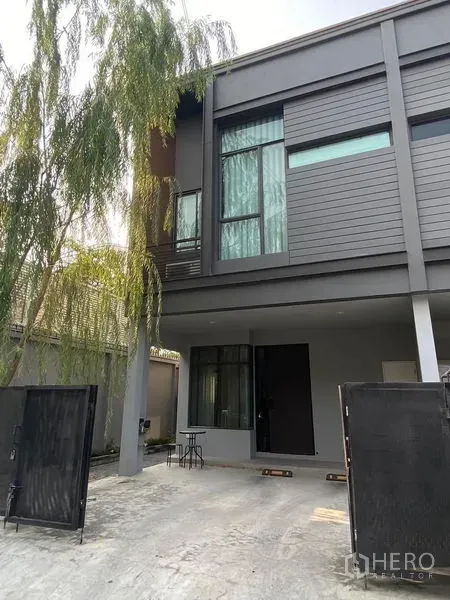 联排别墅 出租在Saphan Sung, Bangkok - 现代两层联排别墅外立面，灰色外墙、高窗，带大门和有顶车位。