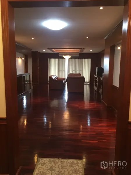 公寓 出租在Watthana, Bangkok - 入口望向宽敞客厅，亮泽木地板、皮沙发、吊灯与落地百叶窗，位于曼谷瓦他那区公寓。