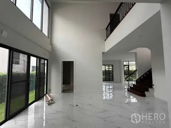 独立式住宅 出售在Lat Krabang, Bangkok - 挑高客厅配落地窗，亮面大理石纹地砖，铁艺栏杆楼梯通向二层。
