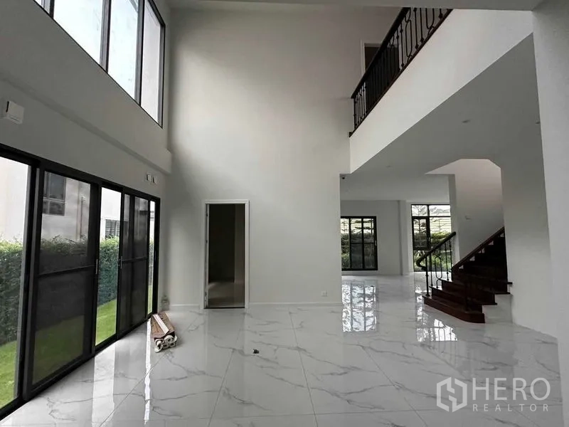 独立式住宅 出售在Lat Krabang, Bangkok - 挑高客厅配落地窗，亮面大理石纹地砖，铁艺栏杆楼梯通向二层。