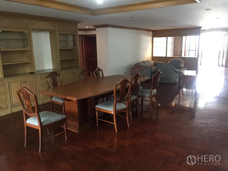 Condominium for rent in Khlong Toei, Bangkok - Open-plan dining and living area with parquet wood floors, built-in cabinetry, and a six-seat table.