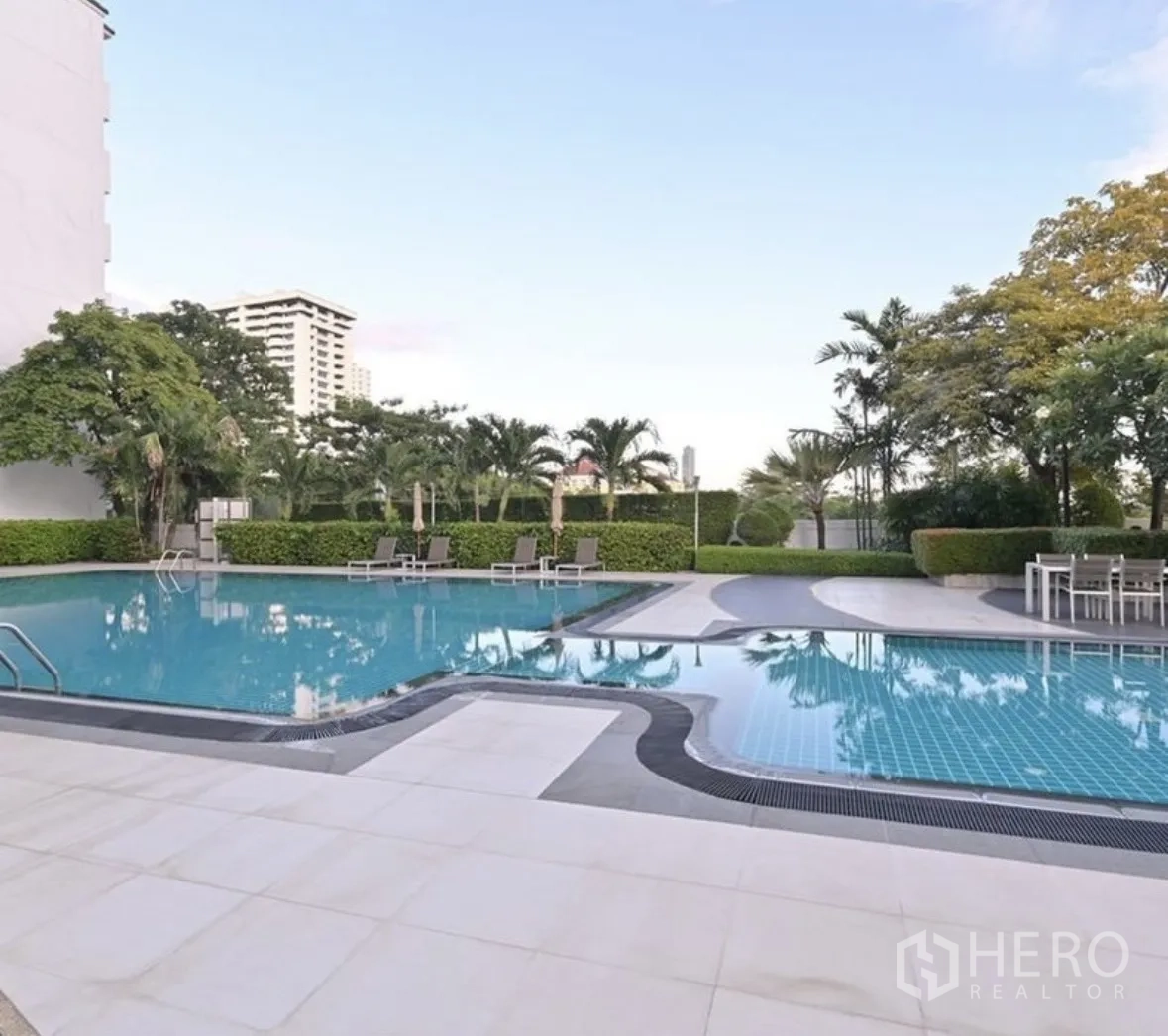 Condominium for rent or sale in Watthana, Bangkok - Outdoor swimming pool with sundeck, loungers, and landscaped greenery.