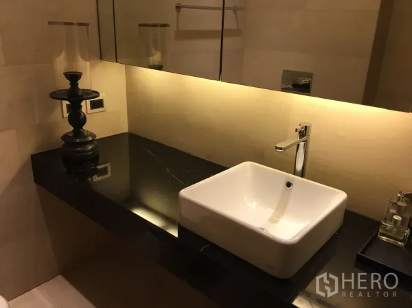 Condominium for rent or sale in Bang Rak, Bangkok - Modern bathroom vanity with square vessel sink on black granite countertop and backlit mirror.