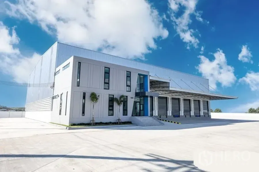 Warehouse for rent in Bang Bo, Samut Prakan - Modern logistics warehouse exterior with office block, multiple loading bays and a wide concrete yard under a blue sky in Bang Bo.