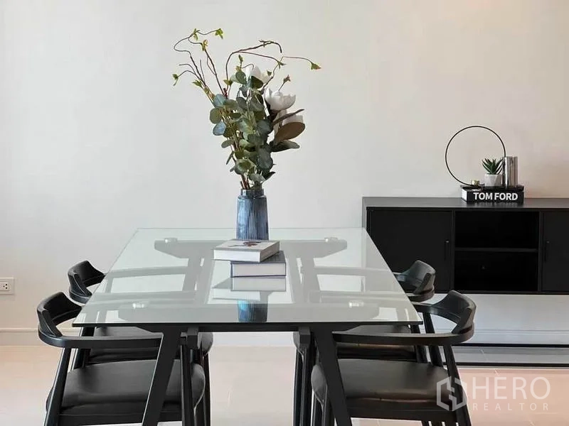 Condominium for rent in Watthana, Bangkok - Minimal dining table with vase centerpiece and low TV console in background.