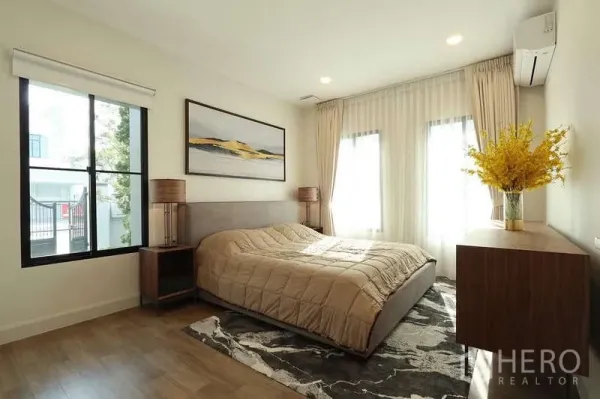 Detached House for rent in Saphan Sung, Bangkok - Cozy bedroom with large windows, wood floors, bedside tables and wall art above the bed.