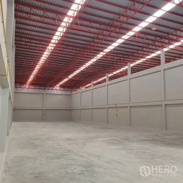 Warehouse for rent in Mueang Samut Sakhon, Samut Sakhon - Spacious warehouse interior with 10–12 m high ceiling, red steel trusses and skylight panels in Mueang Samut Sakhon.