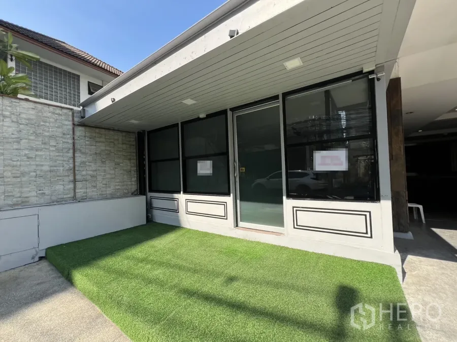 Retail Space for rent in Watthana, Bangkok - Street-facing retail storefront with black-framed glass, sliding door and a small artificial turf forecourt under an awning.