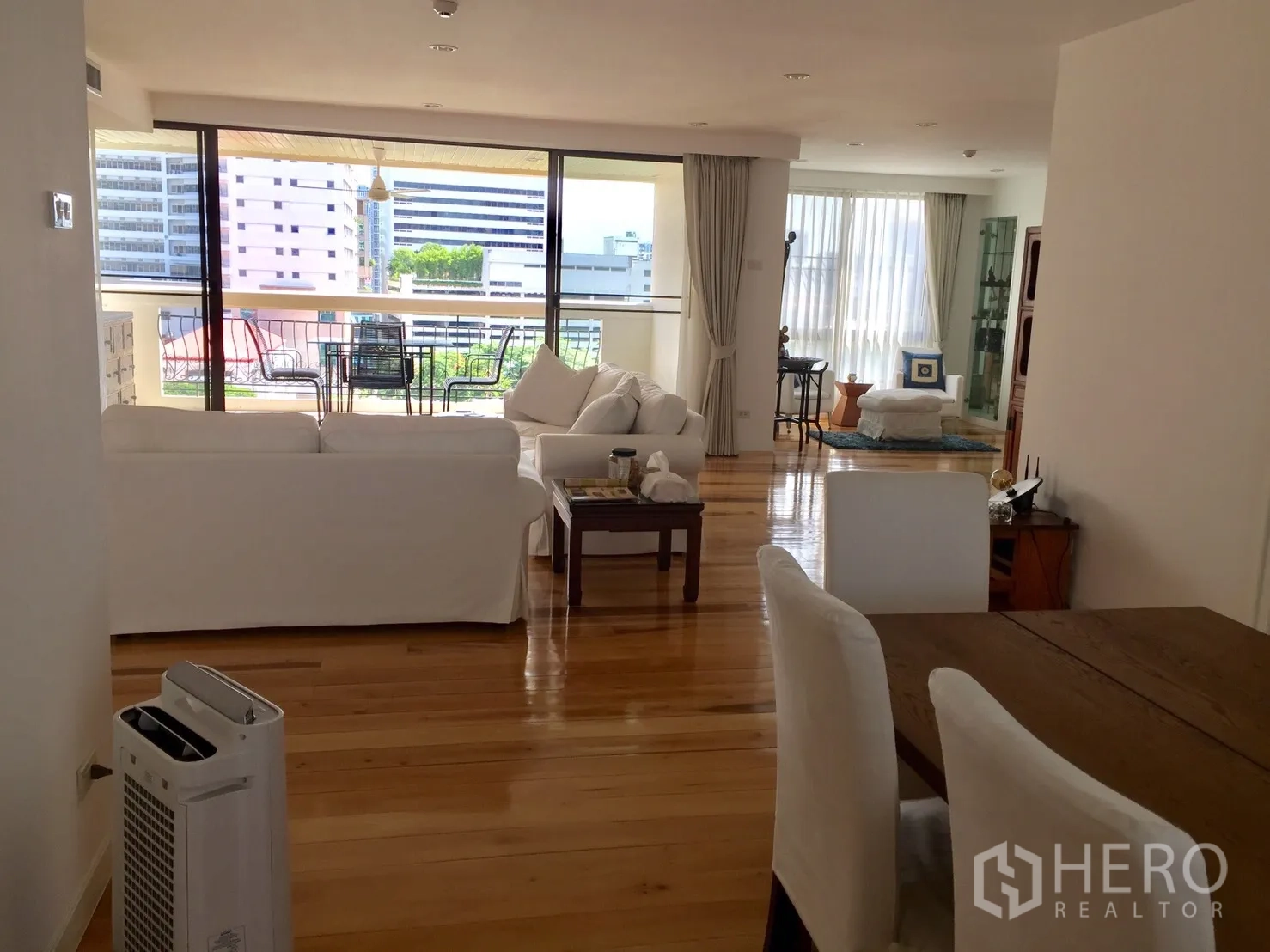 คอนโด ให้เช่าในWatthana, Bangkok - ห้องนั่งเล่นแบบเปิดโล่ง พื้นไม้จริงสวยงาม พร้อมโซฟาสีขาวและระเบียงใหญ่มีชุดโต๊ะทานอาหาร วิวเมือง