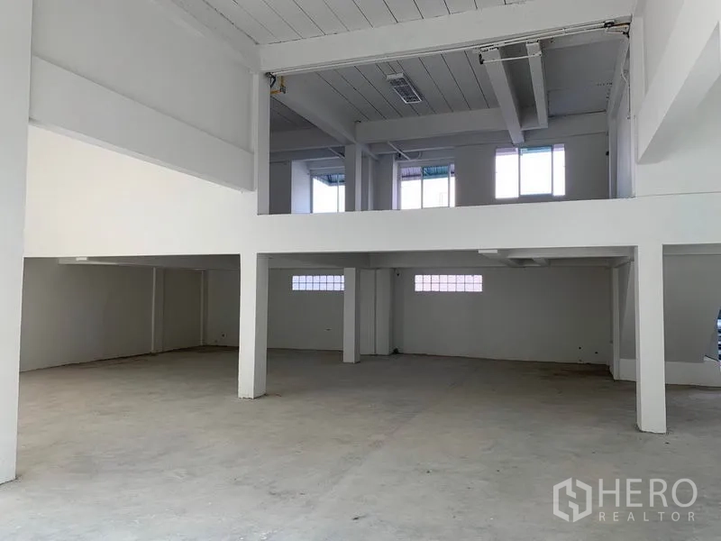 Office Space for rent in Huai Khwang, Bangkok - Double-height hall with mezzanine level, structural columns and a bare concrete floor.