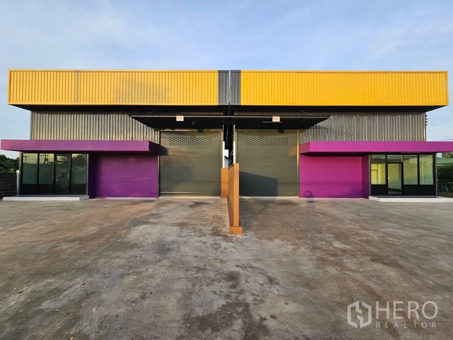 货栈 出租在Lam Luk Ka, Pathum Thani - Lam Luk Ka现代双仓单元外观，黄色金属板与紫色雨棚，双卷闸门，前方大面积混凝土场地。