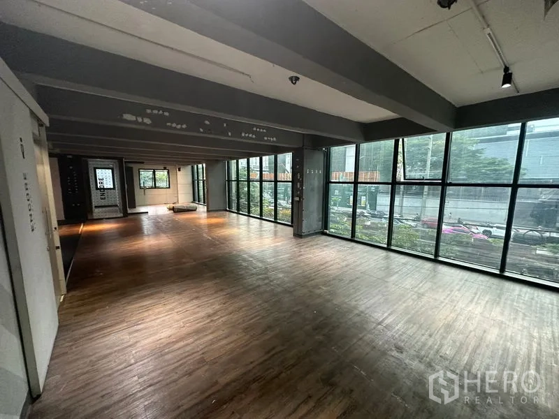 Office Space for rent in Bang Rak, Bangkok - Open-plan office with floor-to-ceiling windows, wood flooring, exposed beams, and city views.